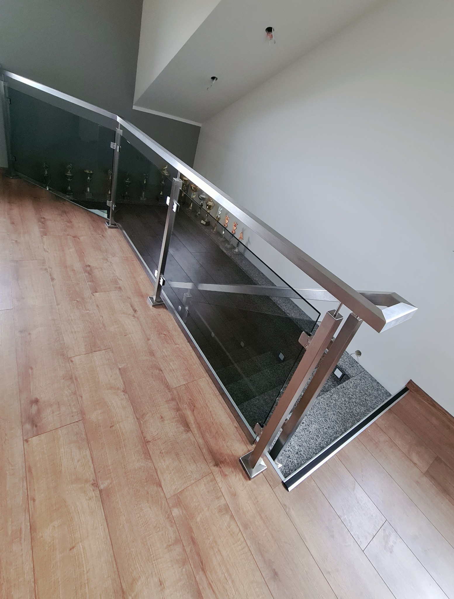 Szklana balustrada ze stalowymi słupkami na schodach wewnątrz budynku, widoczne trofea na półce za szkłem.