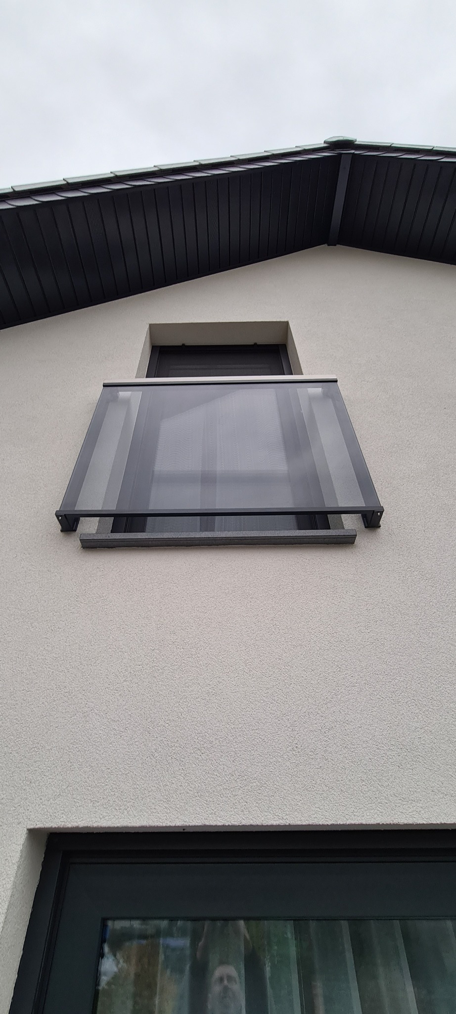 Szklana osłona balkonu z ciemną ramą zamontowana na elewacji budynku, widok z dołu.