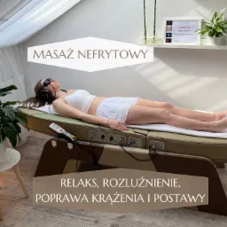 Kobieta relaksuje się na specjalistycznym łóżku do masażu nefrytowego w jasnym wnętrzu. Widoczne certyfikaty i roślina doniczkowa.