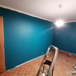 Dominik - Świeżo pomalowane na turkusowo ściany w pokoju, widoczna drabina, podłoga parkietowa, narzędzia malarskie i taśma malarska przy suficie.