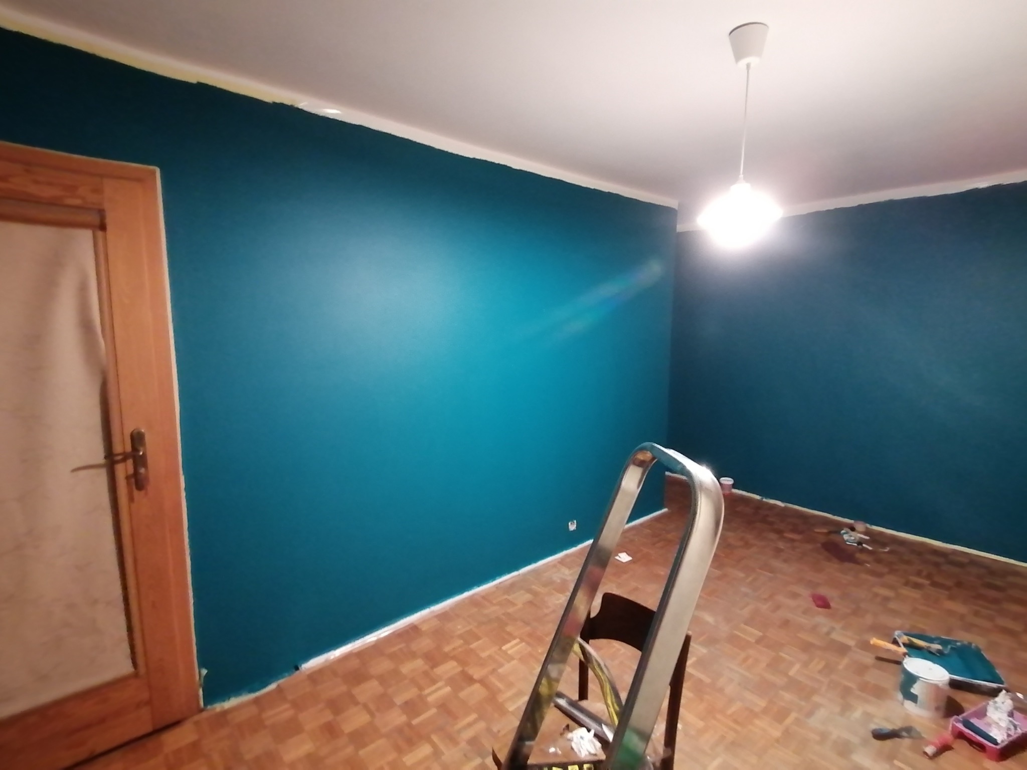 Świeżo pomalowany pokój na turkusowo, widoczna drabina, resztki farby na podłodze, zabezpieczona taśmą odcięcie koloru przy suficie.