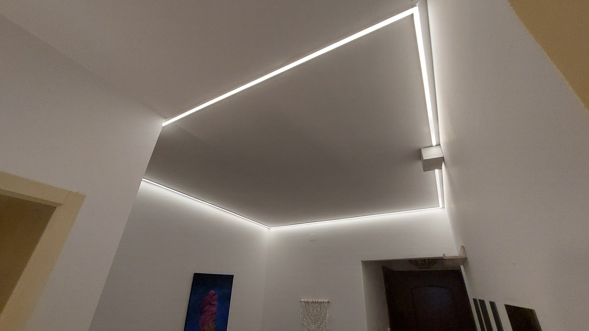 Nowoczesne oświetlenie sufitowe LED w minimalistycznym stylu, zrealizowane w mieszkaniu w Warszawie, widoczne z perspektywy podłogi, z elementami dekoracyjnymi na ścianie.