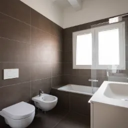 Nowoczesna łazienka z brązowymi płytkami, białymi sanitariatami, wanną i oknem, oświetlona naturalnym światłem.