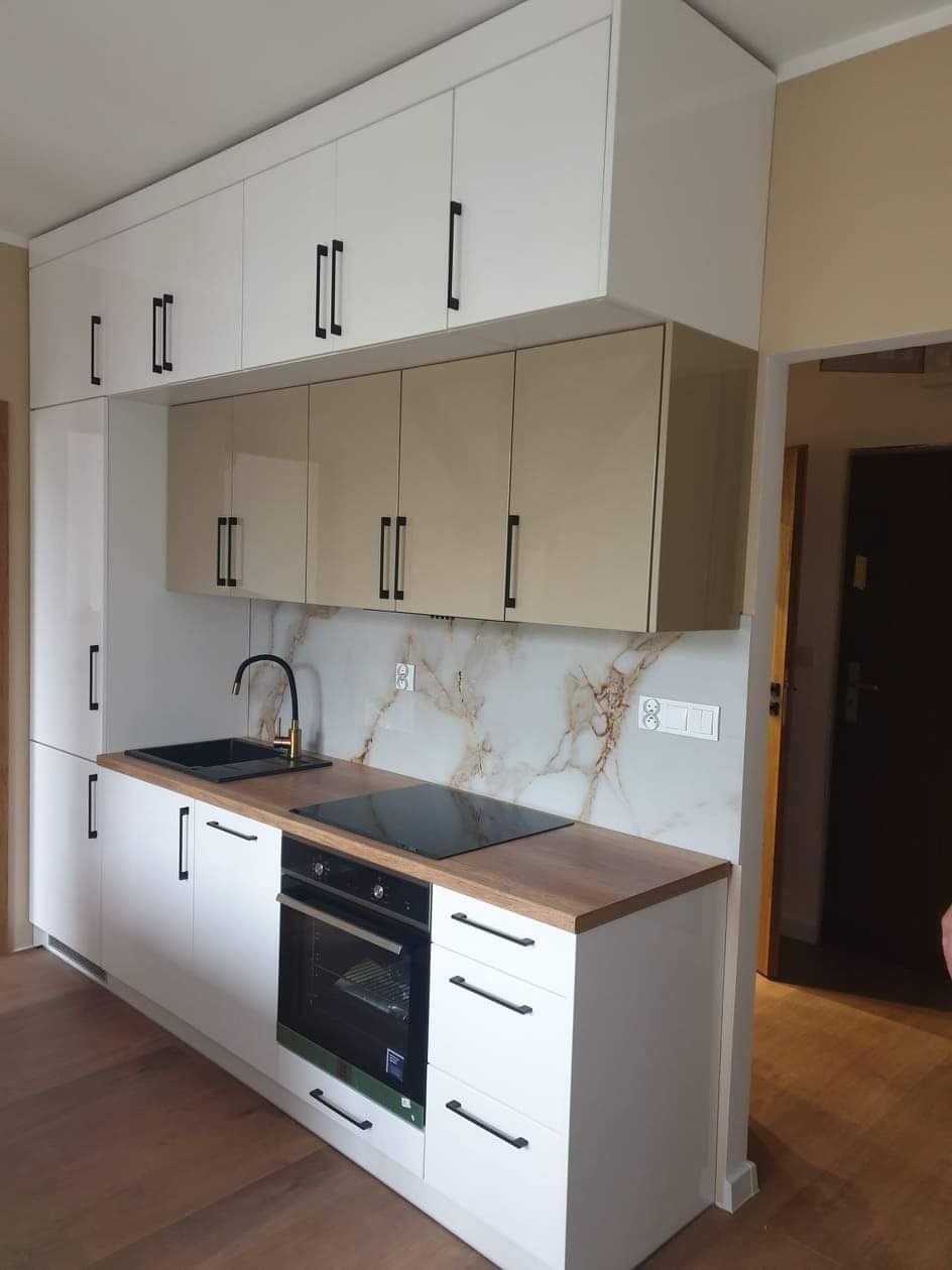 Nowoczesna kuchnia z białymi i beżowymi szafkami, czarnym zlewem i płytą indukcyjną. Marmurowy panel nad blatem. Minimalistyczne uchwyty.