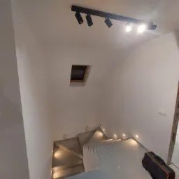 Nowoczesne oświetlenie schodów z punktowymi lampami sufitowymi i wbudowanymi w stopnie w Sosnowcu. Widoczna skrzynka narzędziowa sugeruje trwające prace.