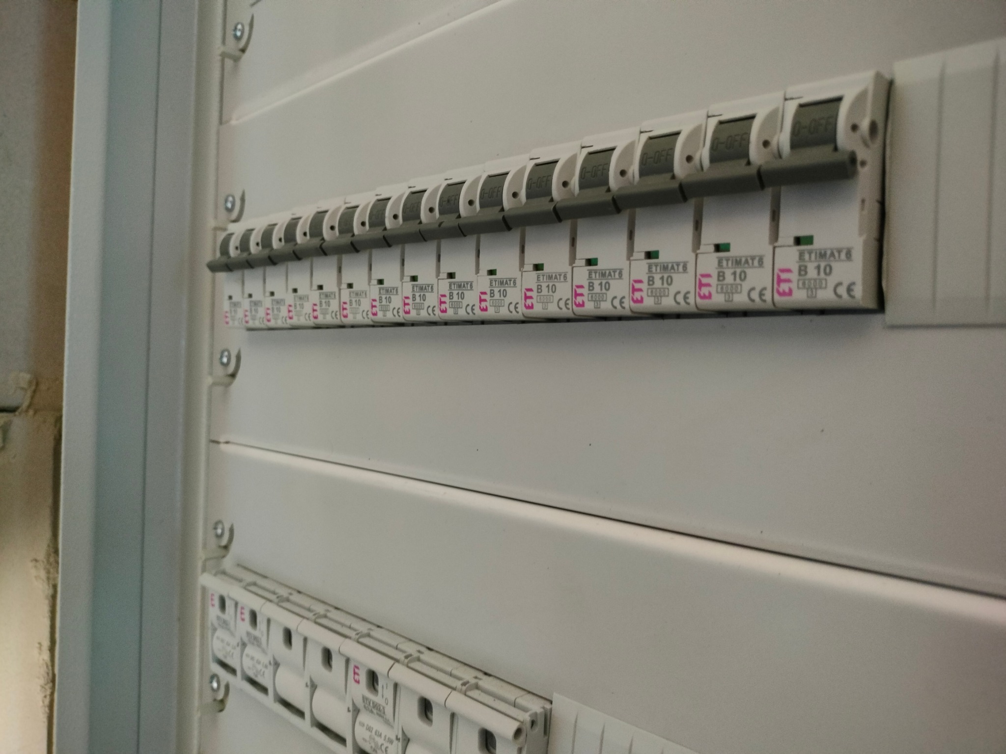Szereg wyłączników nadprądowych ETIMAT B10 w białej skrzynce rozdzielczej, widok z boku pod kątem, część przełączników w pozycji wyłączonej.