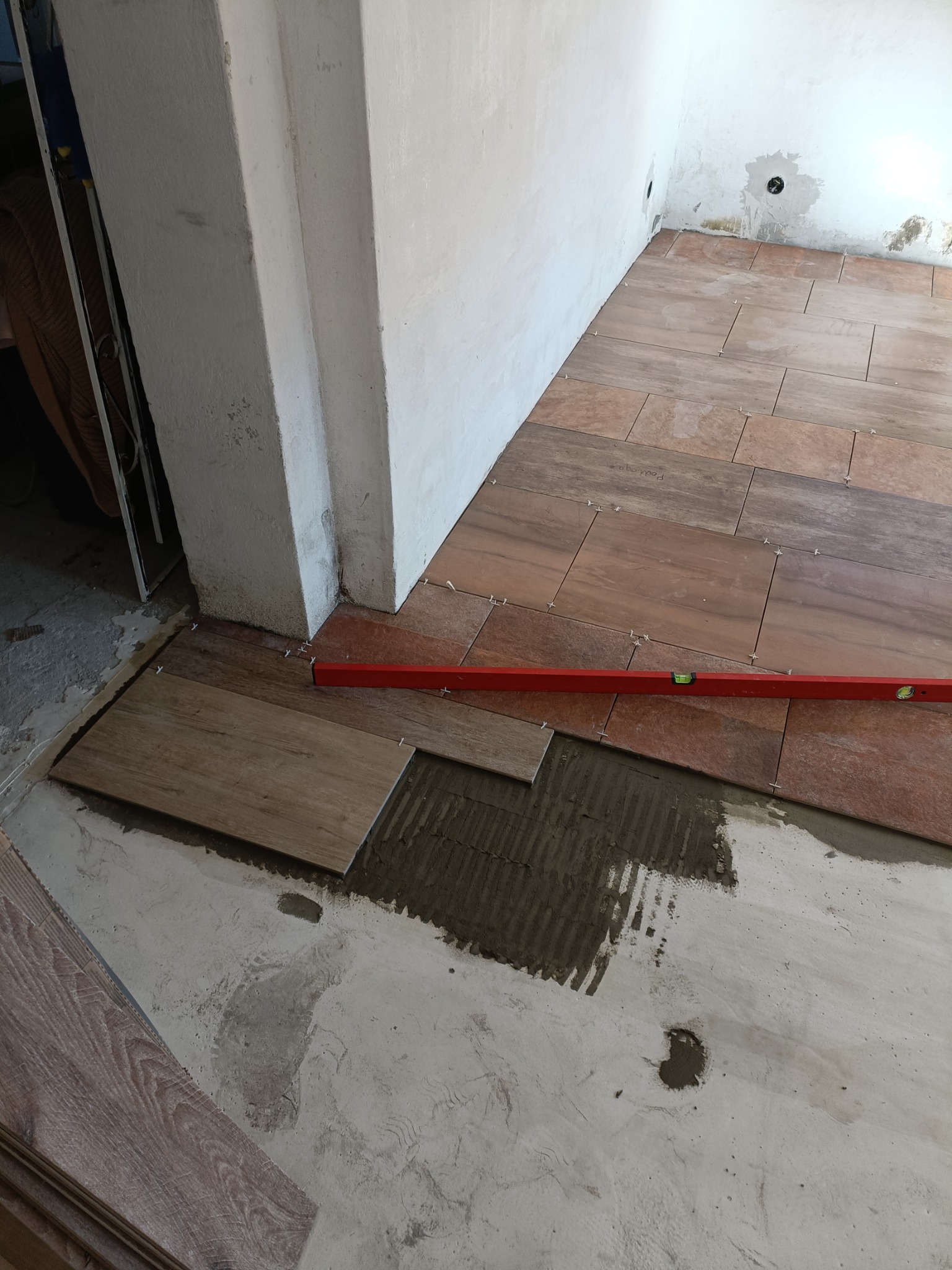 Proces układania podłogi z płytek imitujących drewno, widoczna poziomica i zaprawa klejowa.