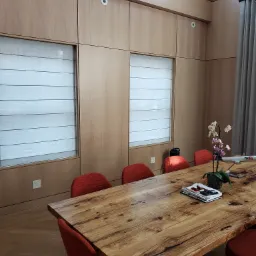 Drewniana sala konferencyjna z długim stołem z litego drewna, czerwonymi krzesłami i zabudową ścienną z ukrytymi roletami.