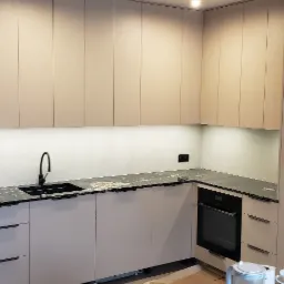 Jasna kuchnia na wymiar z czarnym blatem, minimalistyczny design. Górne szafki podświetlone, widoczny zlew i piekarnik. Nowoczesne wykończenie.