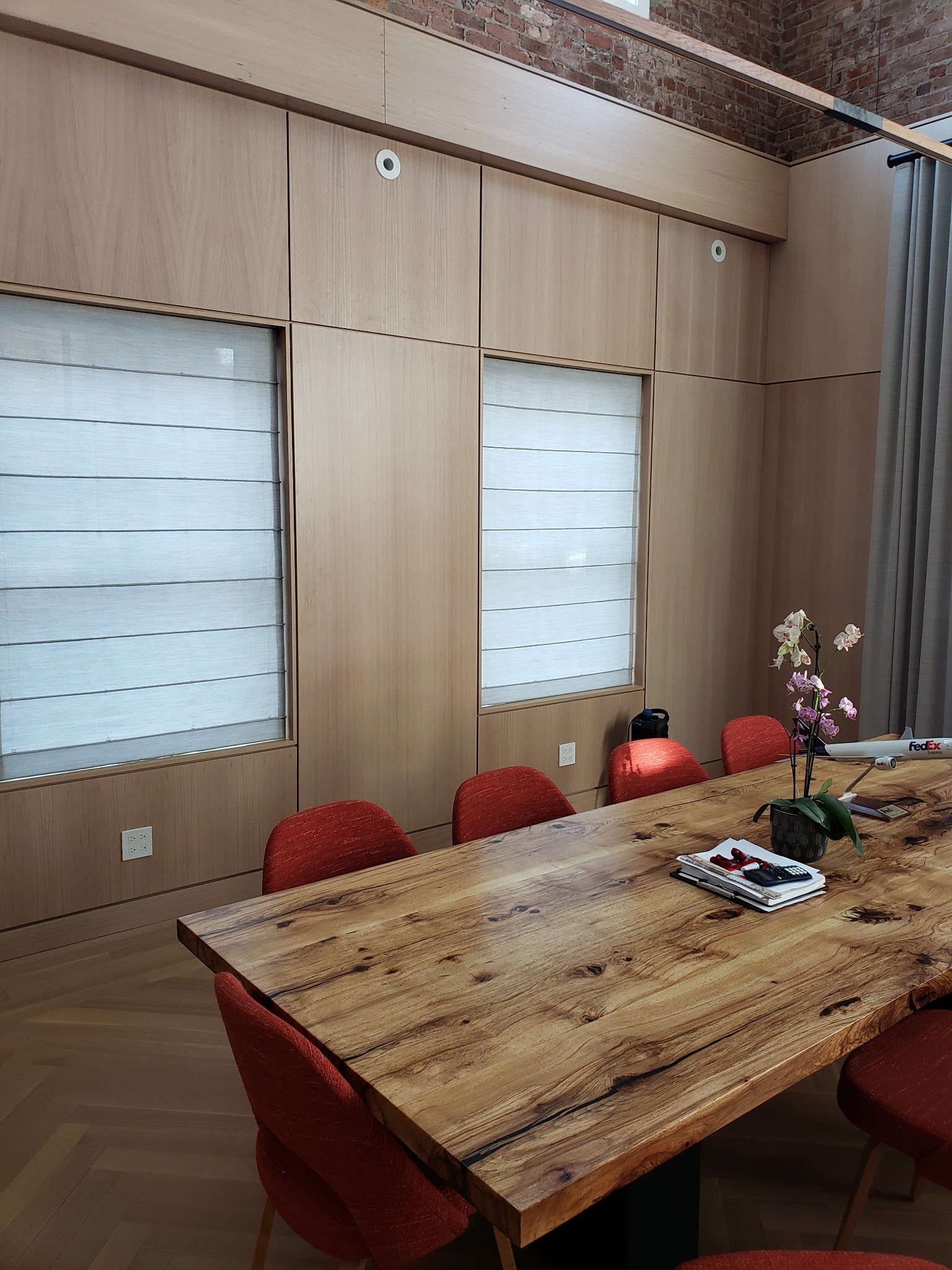 Drewniana sala konferencyjna z długim stołem z litego drewna, czerwonymi krzesłami i zabudową ścienną z ukrytymi roletami.