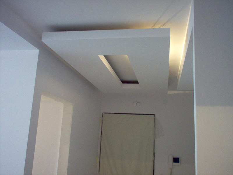 Sufit podwieszany z prostokątnym wgłębieniem i oświetleniem LED, widok z dołu na wykończone wnętrze z drzwiami i ścianami pomalowanymi na biało.