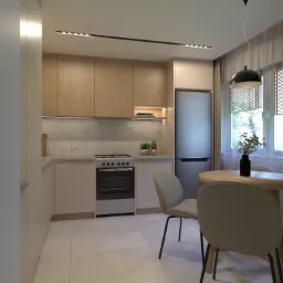 Jasna kuchnia z drewnianymi szafkami, marmurowym backsplashiem i okrągłym stołem z czterema krzesłami. Minimalistyczna lampa wisząca nad stołem. Nowoczesny design.