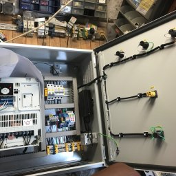 ValKom - Otwarta szafa sterownicza z widocznymi elementami elektrycznymi, w tym przetwornicą częstotliwości, zabezpieczeniami, okablowaniem i schematem elektrycznym na górze. Na tylnej ścianie widoczne...