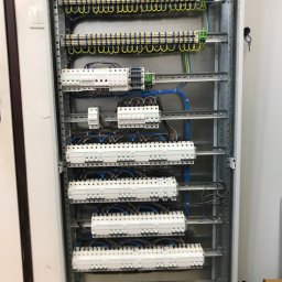 ValKom - Rozdzielnica elektryczna z zamontowanymi bezpiecznikami i listwami zaciskowymi, widoczne kable w kolorach niebieskim, żółtym i zielonym, kluczyk do szafy w zamku.