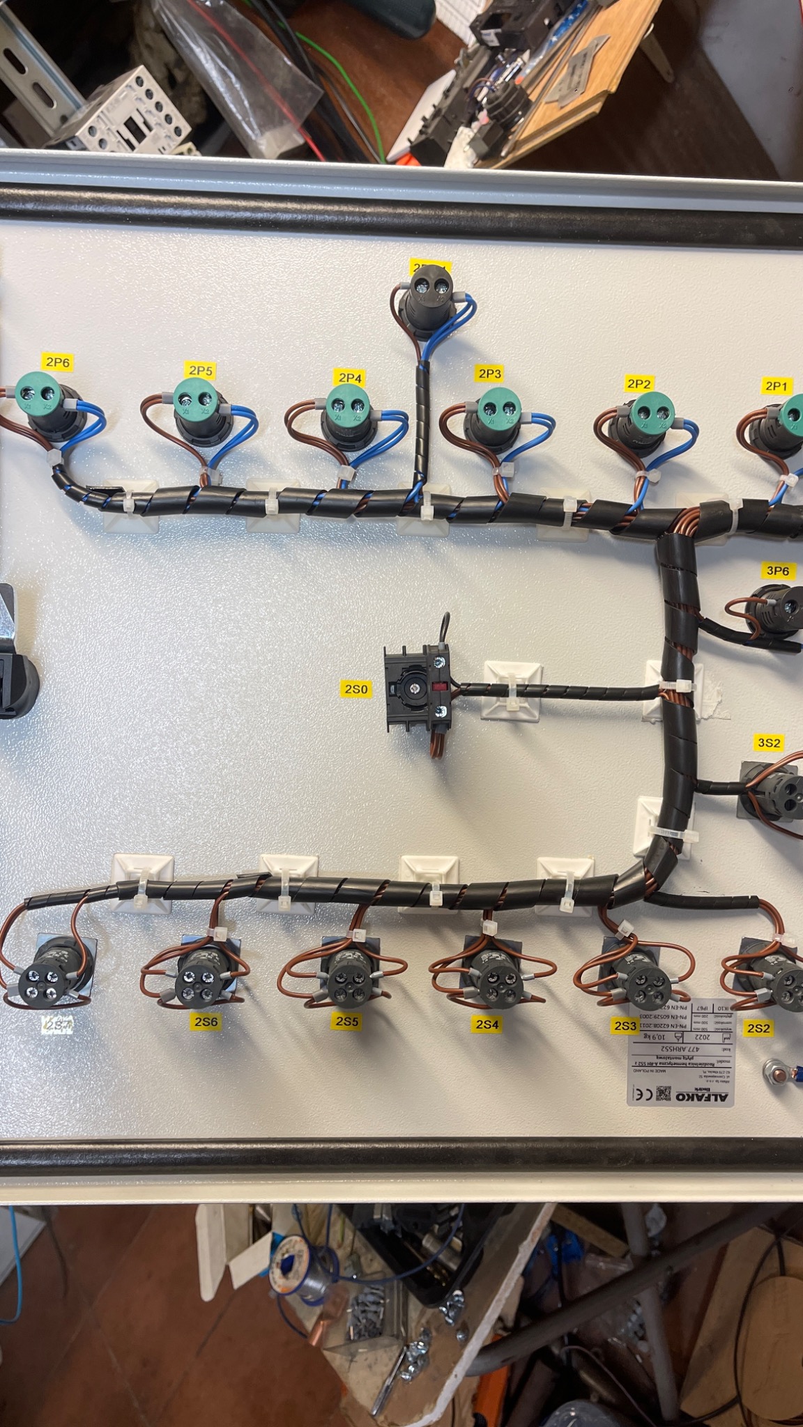 Wnętrze szafy elektrycznej z podłączonymi przewodami, oznaczonymi etykietami 2P1-2P6, 2S0, 2S2-2S6, 3P6 i 3S2, uporządkowane za pomocą spiralnych opasek i uchwytów kablowych, widoczna tabliczka...