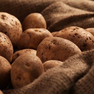 Ziemniaki w jutowym worku, oświetlone ciepłym światłem, z widoczną fakturą skórki i surowego materiału.