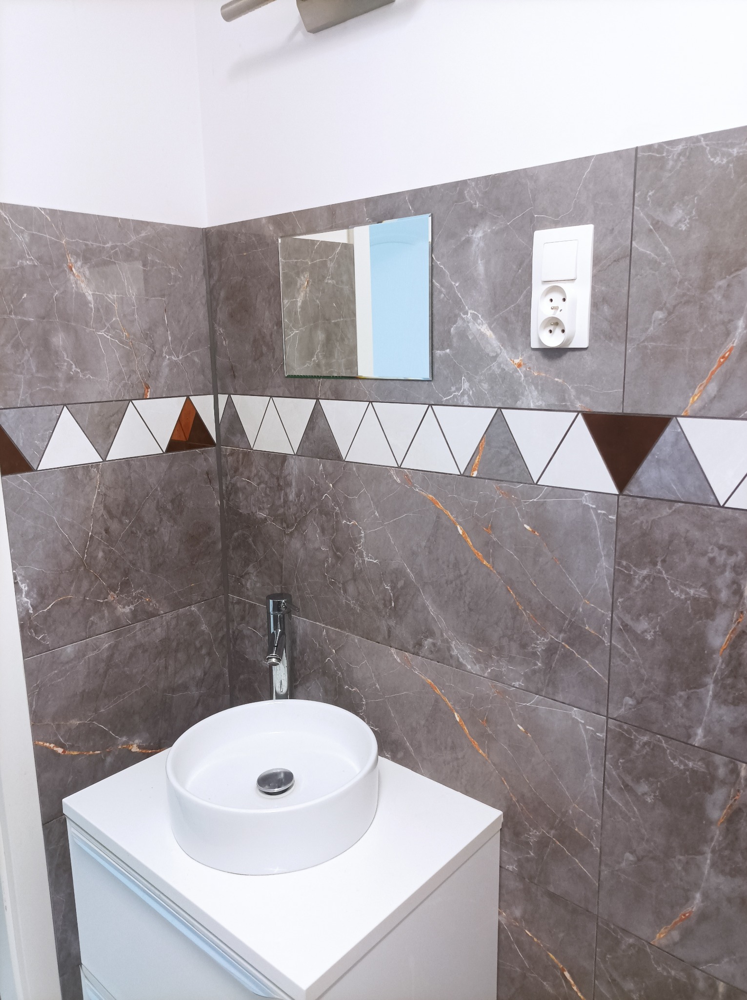 Nowoczesna łazienka w Komornikach z szarymi płytkami imitującymi marmur, dekoracyjnym pasem trójkątnych płytek i okrągłą umywalką nablatową na białej szafce.