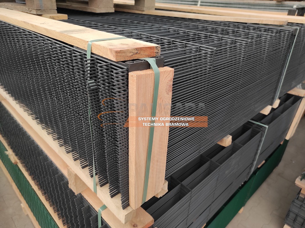 Stos paneli ogrodzeniowych z drutu w kolorze grafitowym, zabezpieczonych drewnianymi belkami i taśmą, przygotowanych do transportu w Gzin.