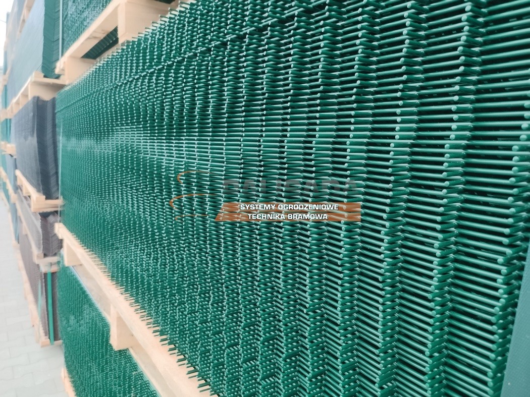 Stos zielonych, spawanych paneli ogrodzeniowych na drewnianych paletach, widoczne logo producenta.