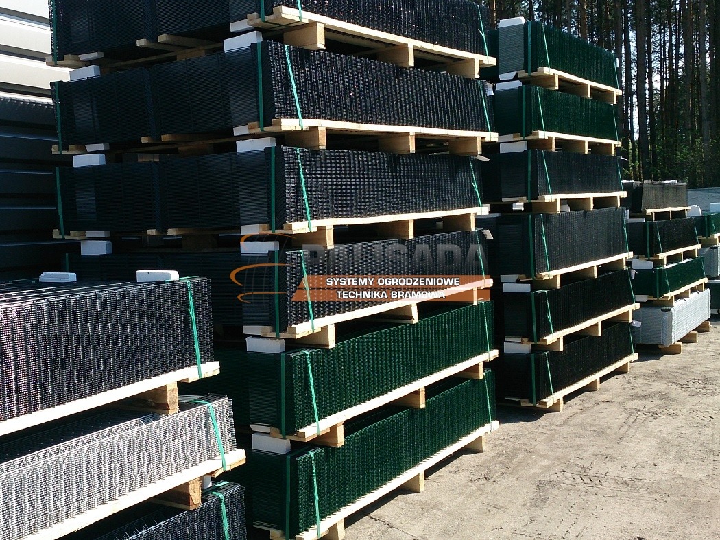 Stosy paneli ogrodzeniowych metalowych w kolorze czarnym, zielonym i szarym, ułożone na drewnianych paletach, przygotowane do transportu, widok z boku.