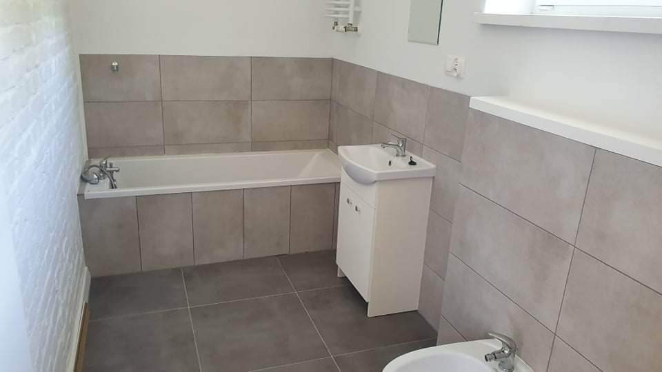 Wyremontowana łazienka z szarymi płytkami, białą wanną i szafką pod umywalką oraz bidetem.