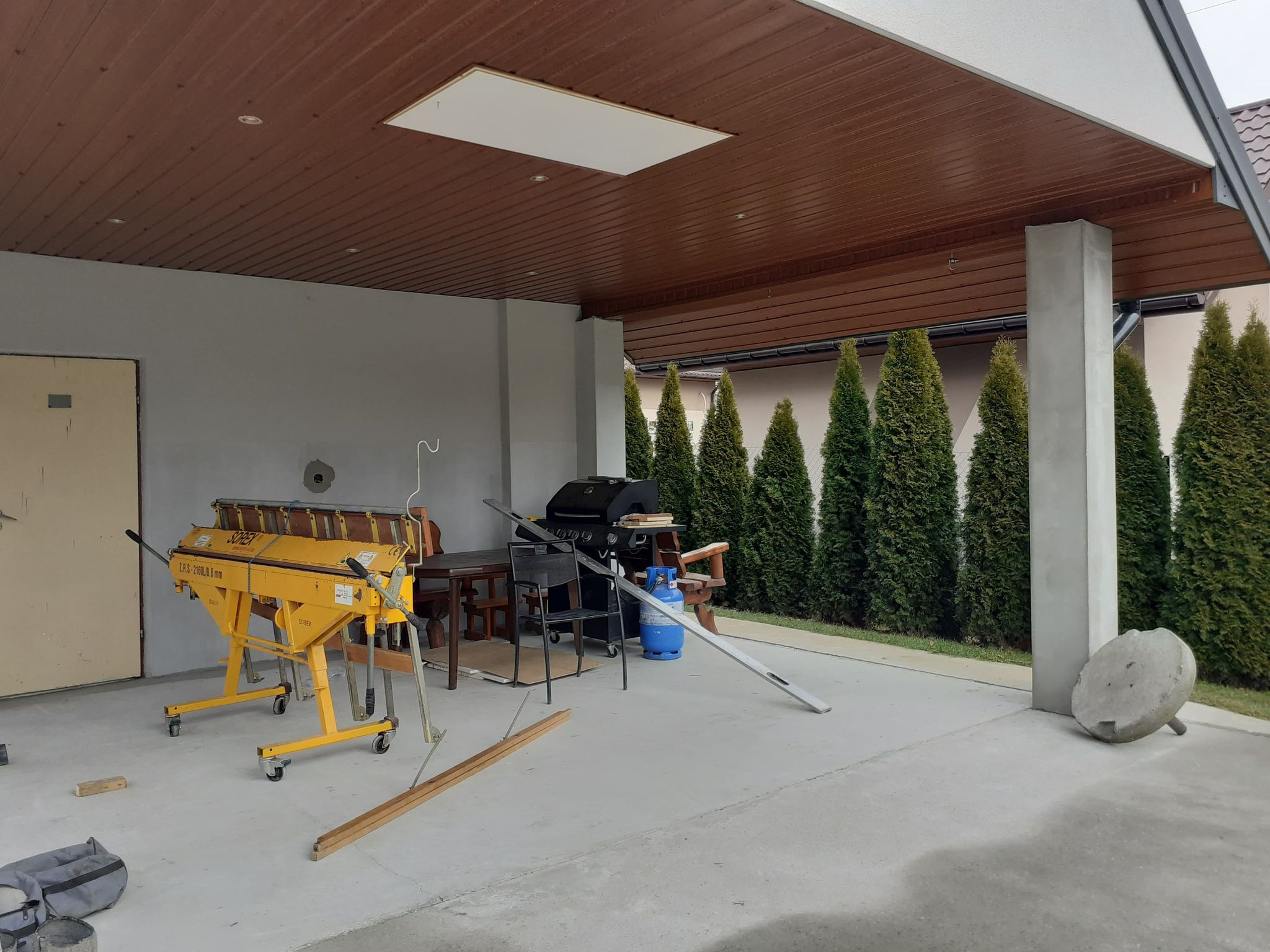 Żółta zaginarka dekarska Sorex na kółkach, butla gazowa i grill na zadaszonym tarasie w Wietrzychowicach, przygotowania do prac blacharskich.