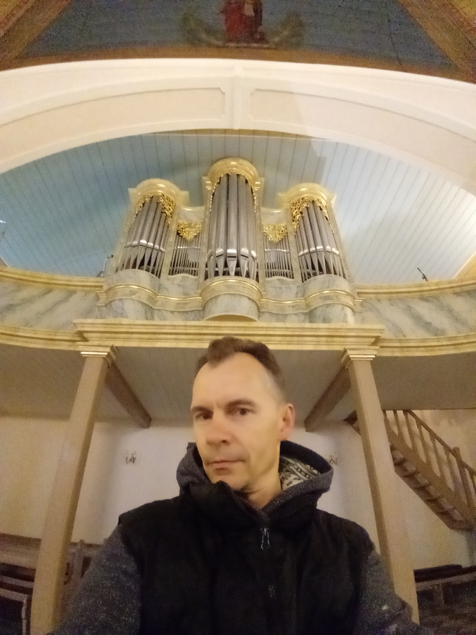 Mężczyzna robiący selfie na tle organów w kościele z odrestaurowanym sufitem i ścianami.