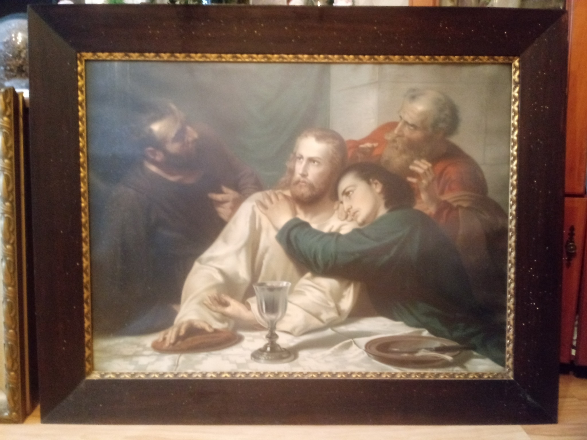 Oprawiony obraz przedstawiający scenę Ostatniej Wieczerzy, z widoczną szklanką na stole i czterema postaciami, w tym jedną opierającą się o ramię centralnej postaci.