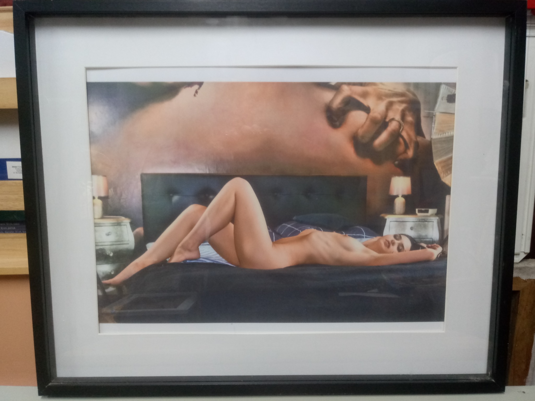 Oprawiony obraz przedstawia nagą kobietę leżącą na łóżku na tle malowidła ściennego przedstawiającego fragment Stworzenia Adama Michała Anioła.