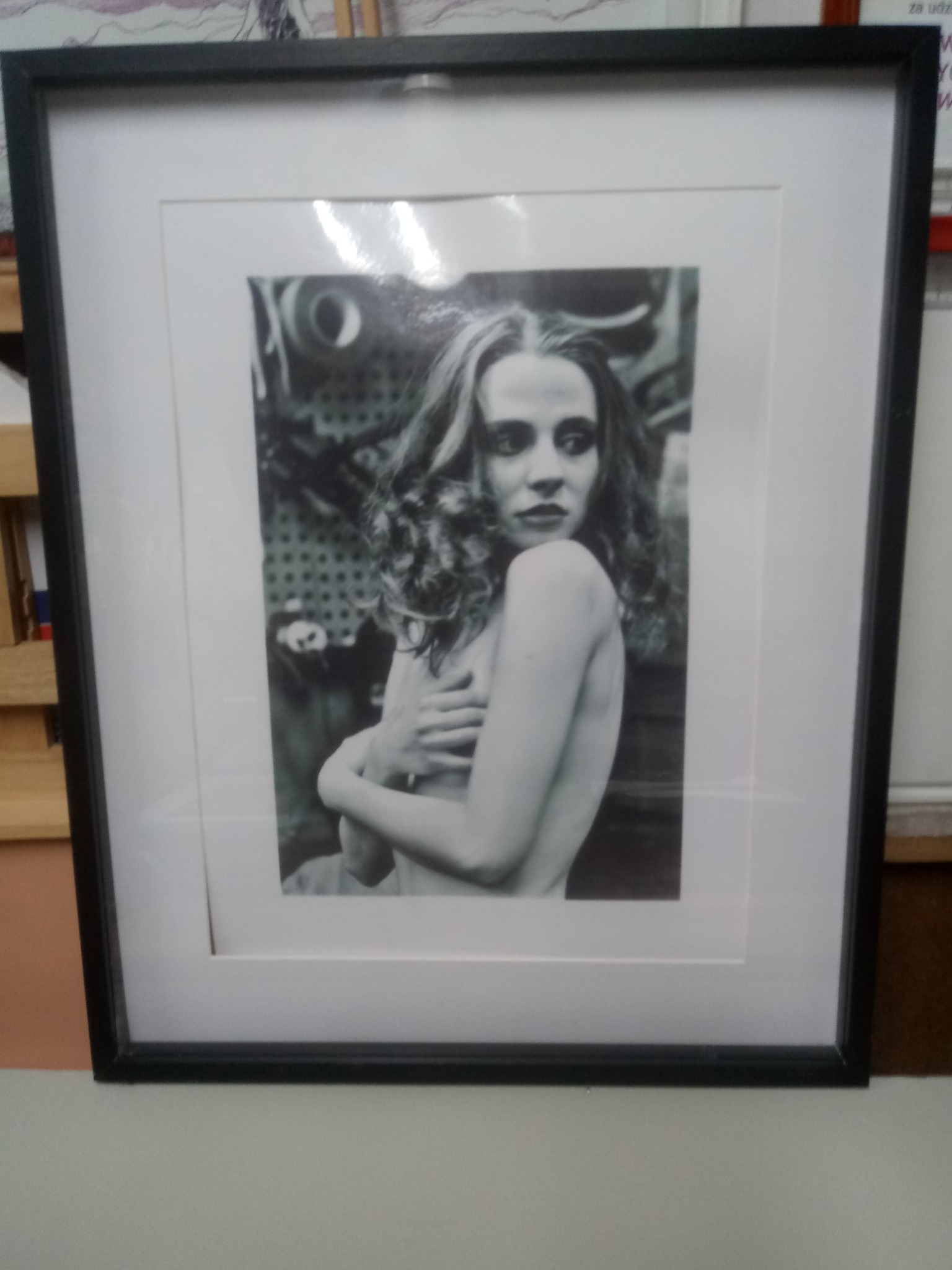 Oprawiona w czarną ramę fotografia czarno-biała przedstawiająca portret kobiety z kręconymi włosami, z industrialnym tłem.