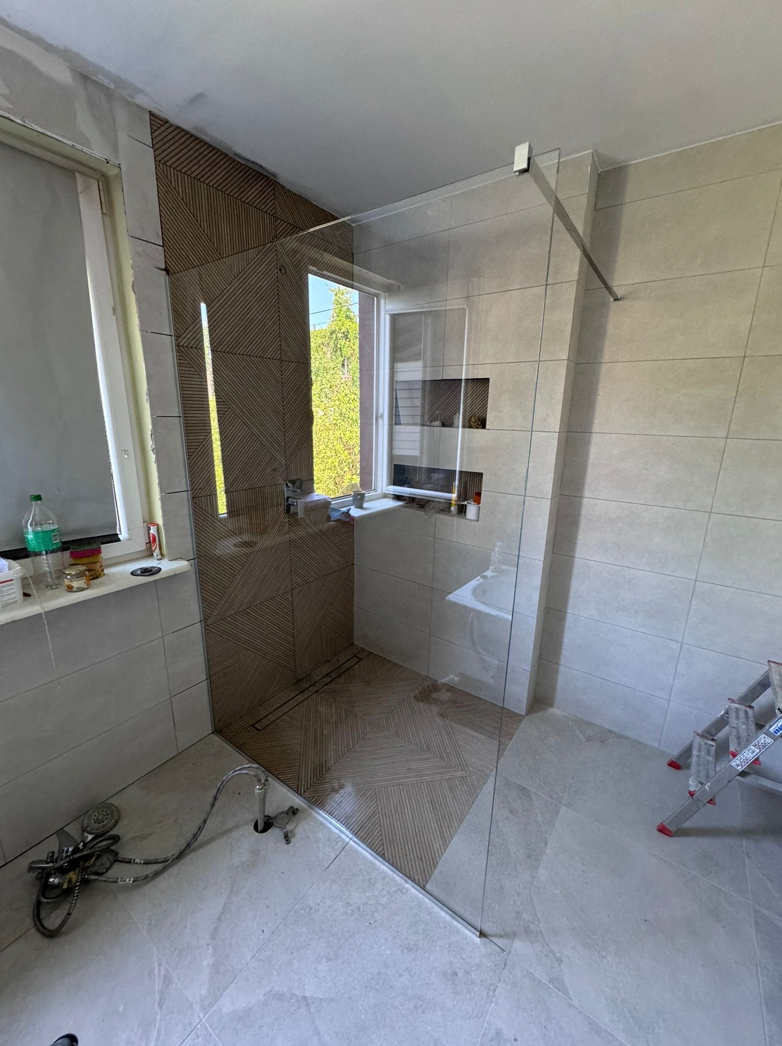 Montaż kabiny prysznicowej ze szklaną ścianką, widoczne narzędzia i nieukończone prace wykończeniowe.