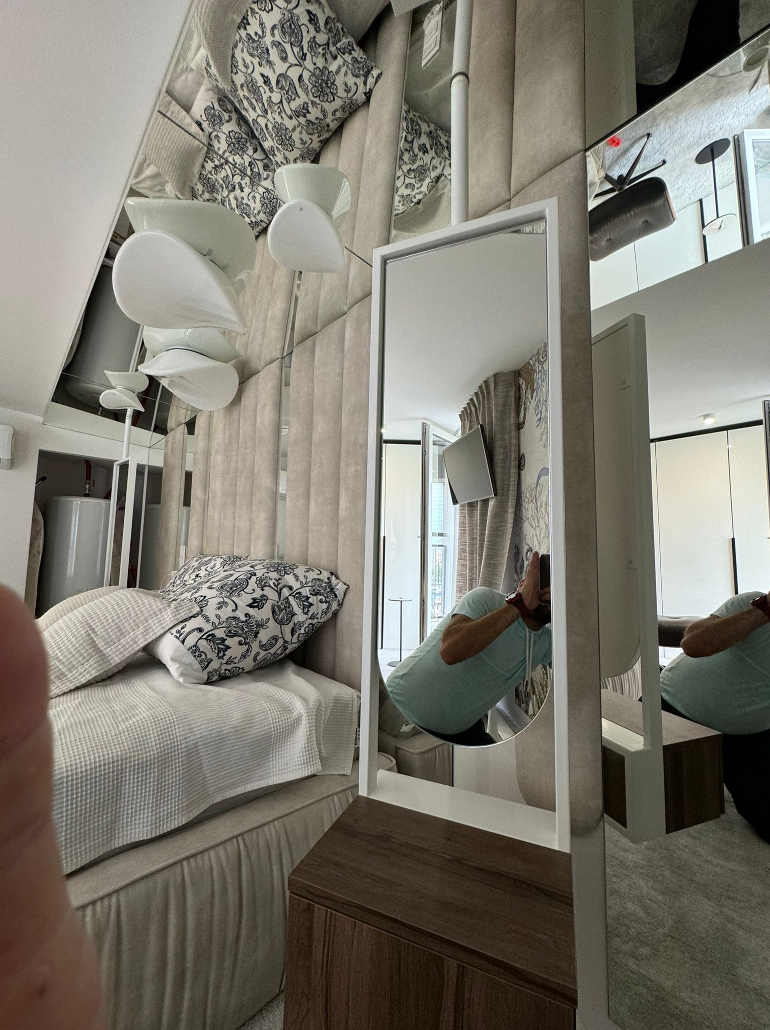 Nowoczesna sypialnia z lustrzaną ścianą i białym lustrem w białej ramie, odbijającym fragment osoby robiącej zdjęcie