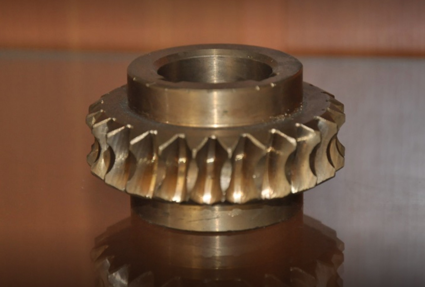 Metalowa zębatka o skomplikowanym kształcie zębów, leżąca na błyszczącej powierzchni, odbijająca swoje światło.