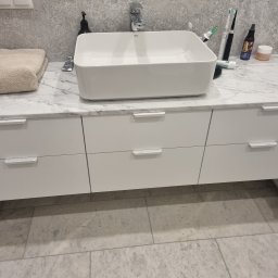 SONO MEBLE - Nowoczesna łazienka z białą umywalką nablatową Roca na szafce z szufladami. Marmurowy blat i podłoga. Minimalistyczny design, eleganckie wykończenie.
