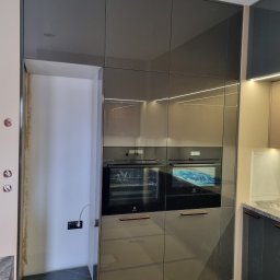 SONO MEBLE - Szare, lakierowane fronty zabudowy kuchennej z wbudowanymi piekarnikami Electrolux, oświetlenie LED pod szafkami. Widoczny fragment ściany z gniazdkami.