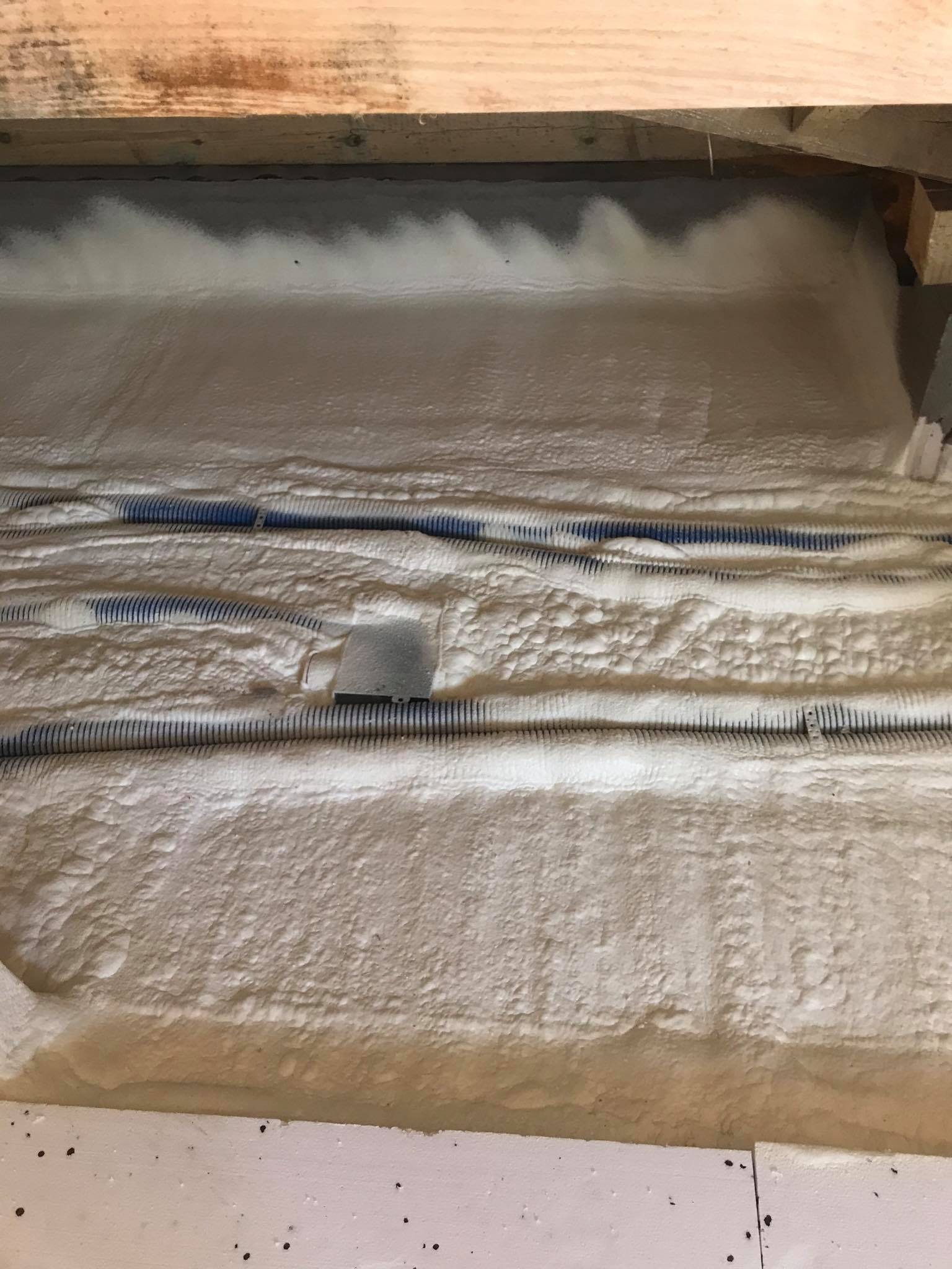 Poddasze ocieplone białą pianką PUR, widoczne kable w peszlach zatopione w izolacji, drewniana belka stropowa u góry kadru.