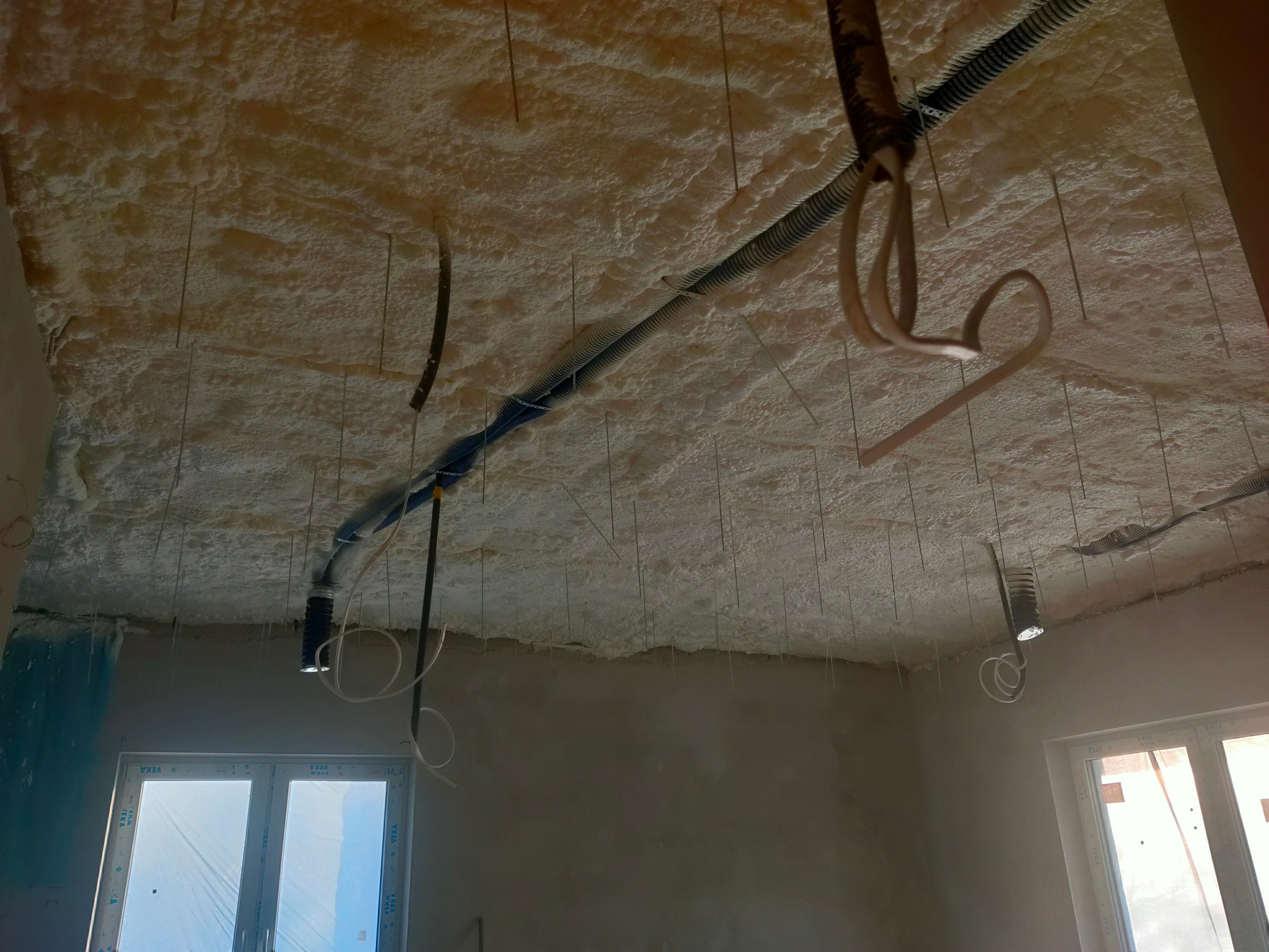 Poddasze po ociepleniu pianką PUR, widoczne kable i przewody instalacyjne przymocowane do sufitu, okno z folią ochronną w tle.