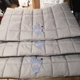 CustoMove - Stos trzech szarych, pikowanych mat z wyhaftowanym logo firmy dla psów, każda z innym imieniem: Bajka, Ramzes, Bianca.
