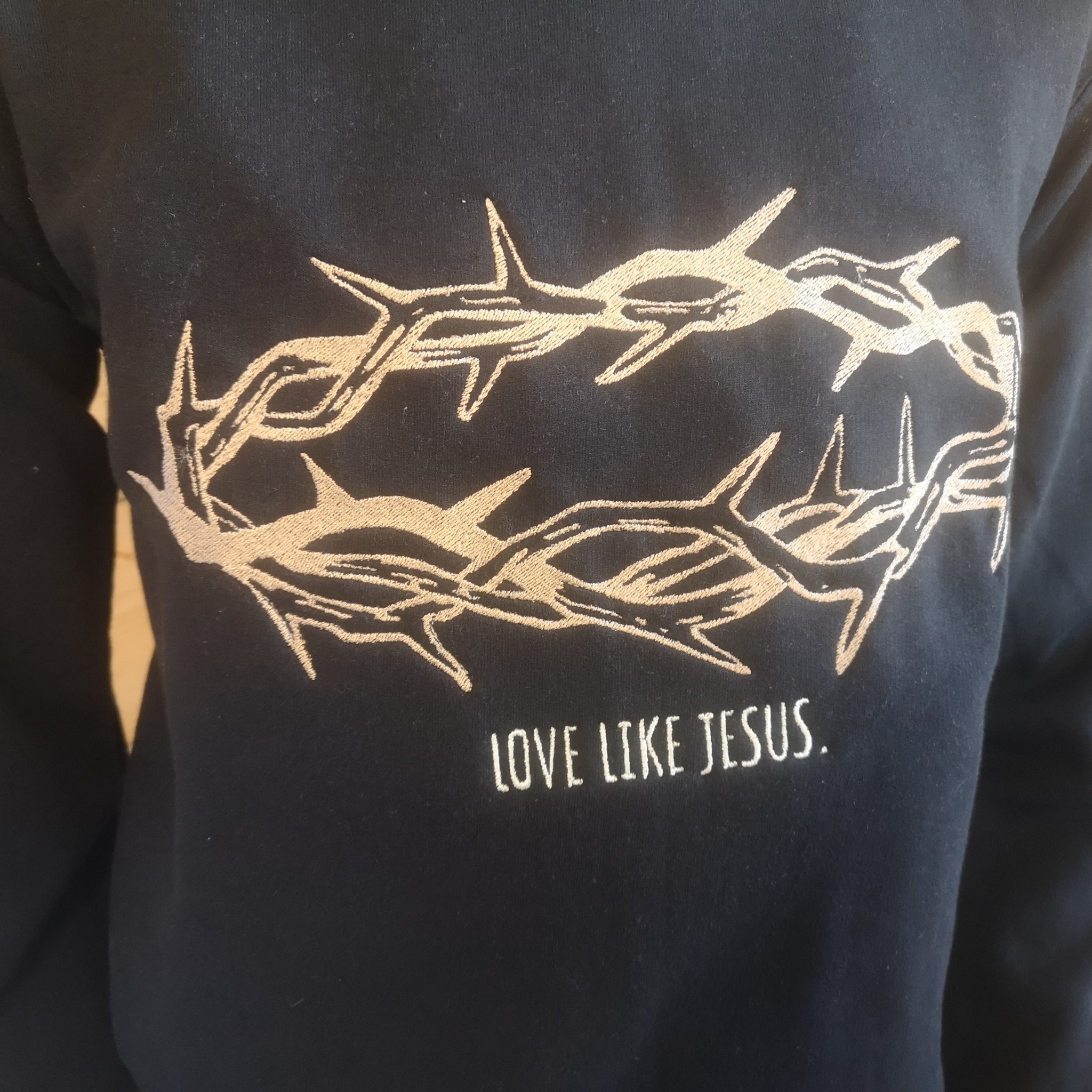 Ciemna bluza z haftowanym motywem korony cierniowej i napisem 'LOVE LIKE JESUS.'