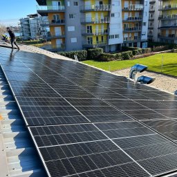 MS SOLAR ENERGY Sp. z o.o. - Instalacja paneli słonecznych na dachu budynku mieszkalnego w słoneczny dzień. Widoczni pracownicy w trakcie montażu, panele Maysun Solar oraz elementy wentylacji dachowej. W tle budynek mieszkalny...