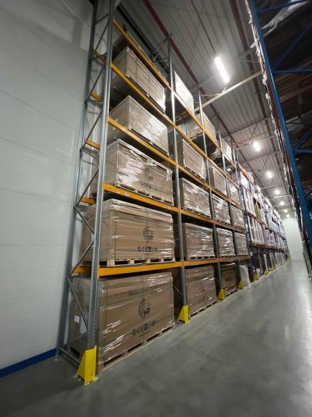 Magazyn Rhenus Logistics w Radonice: Rzędy regałów wypełnione paletami z panelami słonecznymi Maysun Solar, zabezpieczonymi folią stretch, z żółtymi osłonami dolnych słupków regałów.