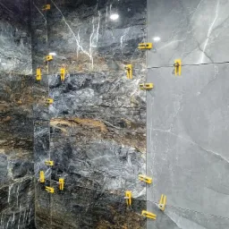 Montaż płytek imitujących marmur w łazience, z użyciem żółtych klipsów poziomujących na sznurku. Dwie ściany wyłożone różnymi wzorami płytek.