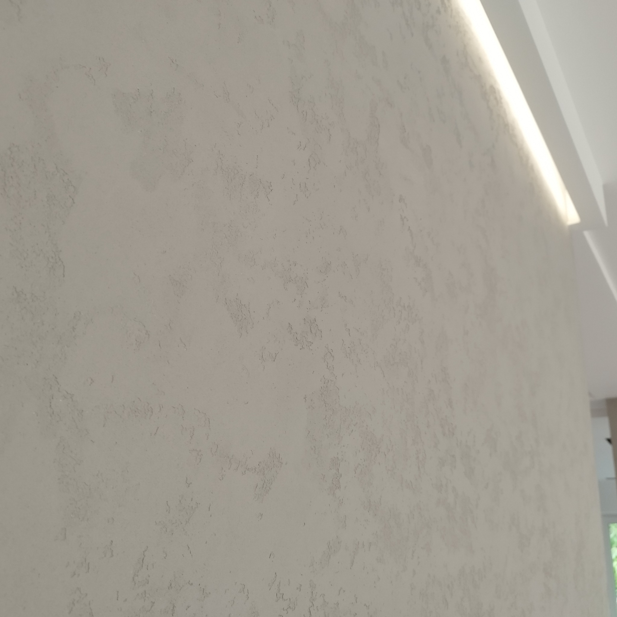 Ściana pokryta szarą, dekoracyjną gładzią strukturalną z oświetleniem LED wzdłuż sufitu, widok z boku.