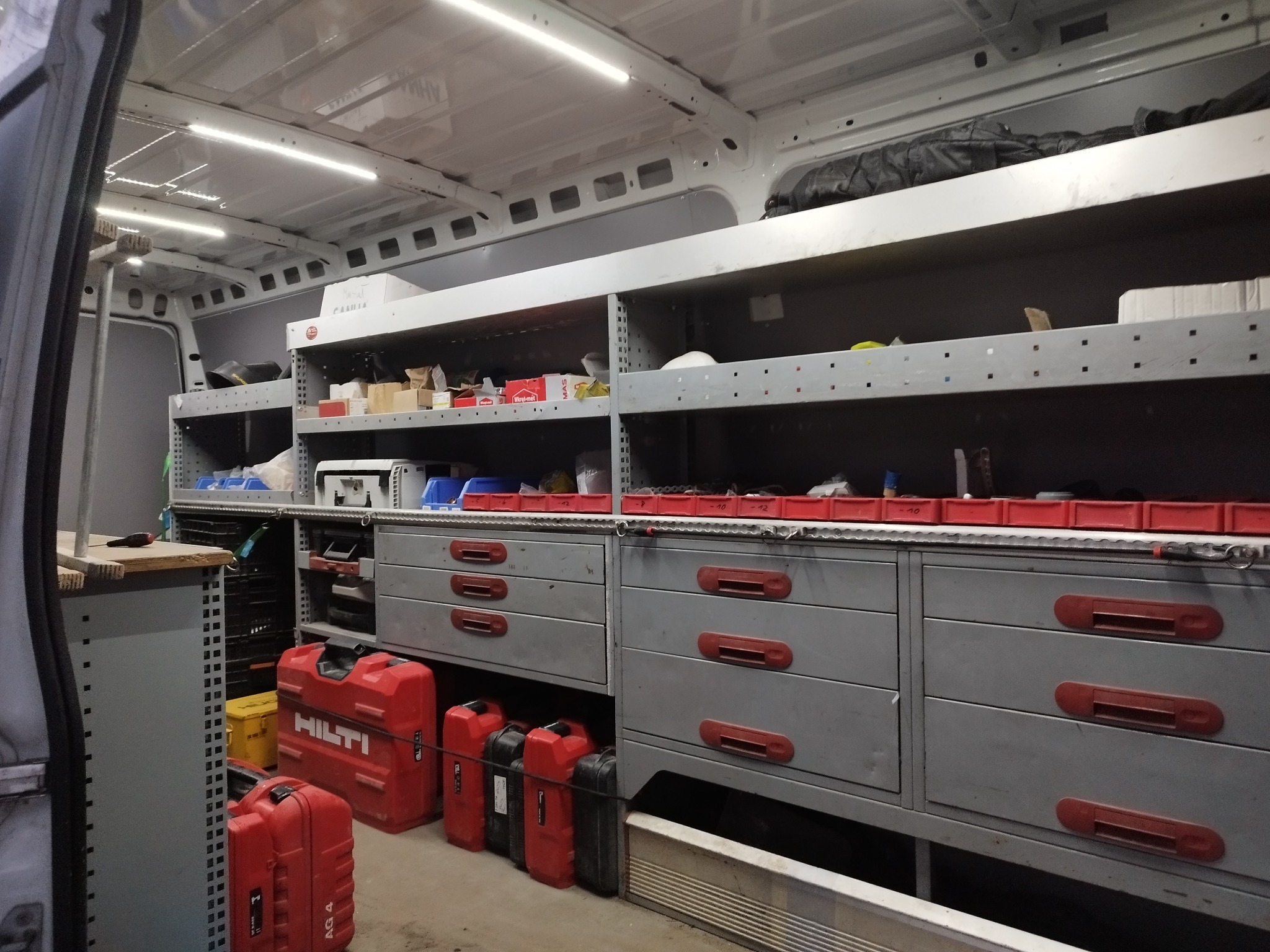 Wnętrze furgonetki serwisowej z zamontowanymi szufladami, półkami i skrzynkami narzędziowymi, widoczne skrzynki Hilti.