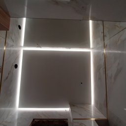 Karol Matuszewski - Wykończone wnętrze z marmurową okładziną, oświetleniem LED w formie kwadratu na suficie i złotymi listwami dekoracyjnymi.