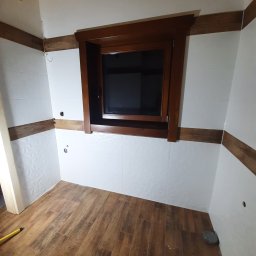 Karol Matuszewski - Wykończona łazienka z drewnopodobną podłogą i białymi płytkami ściennymi z delikatnym wzorem, drewniane obramowanie okna i listwy na ścianach.