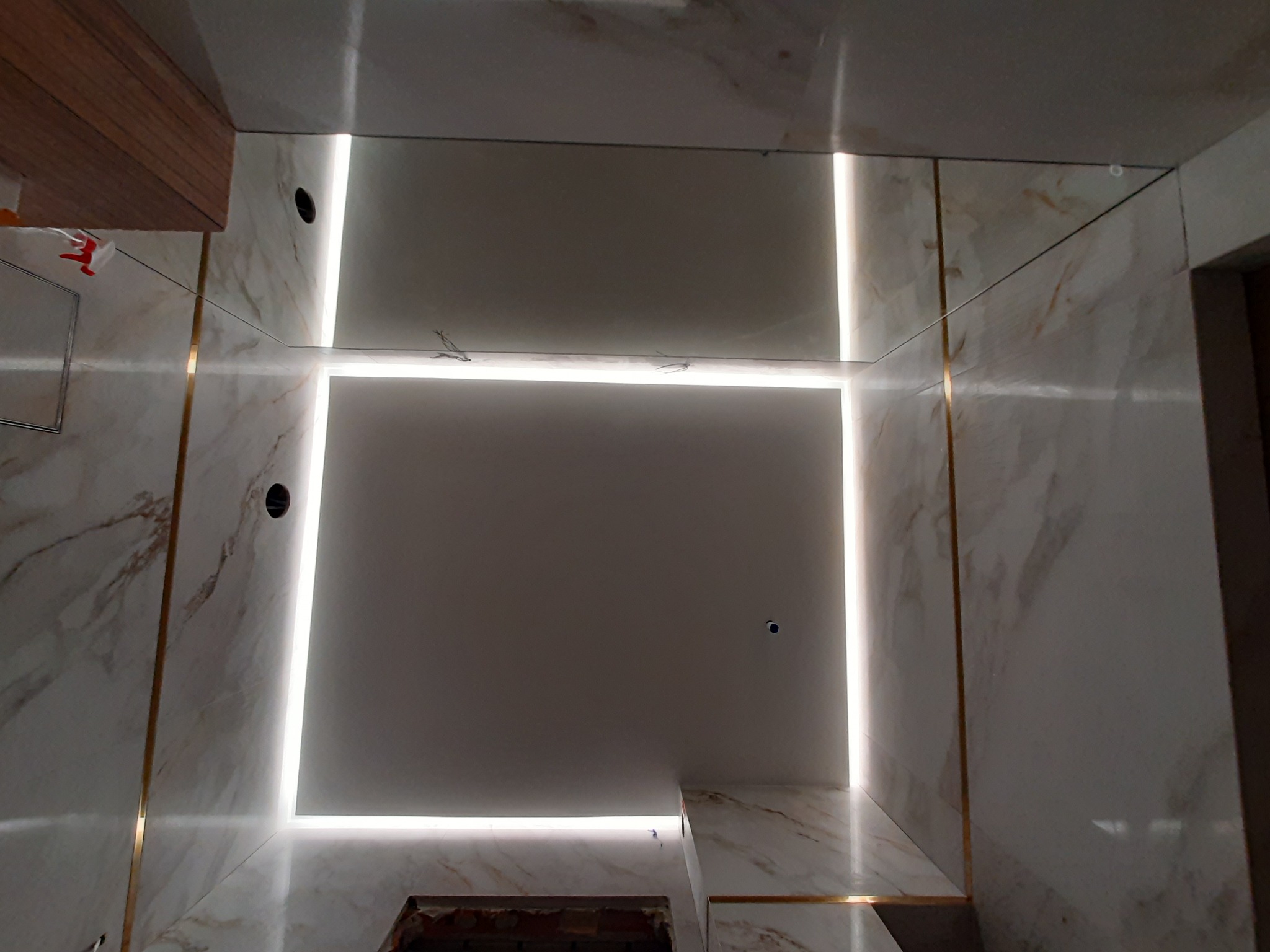 Wykończone wnętrze z marmurową okładziną, oświetleniem LED w formie kwadratu na suficie i złotymi listwami dekoracyjnymi.