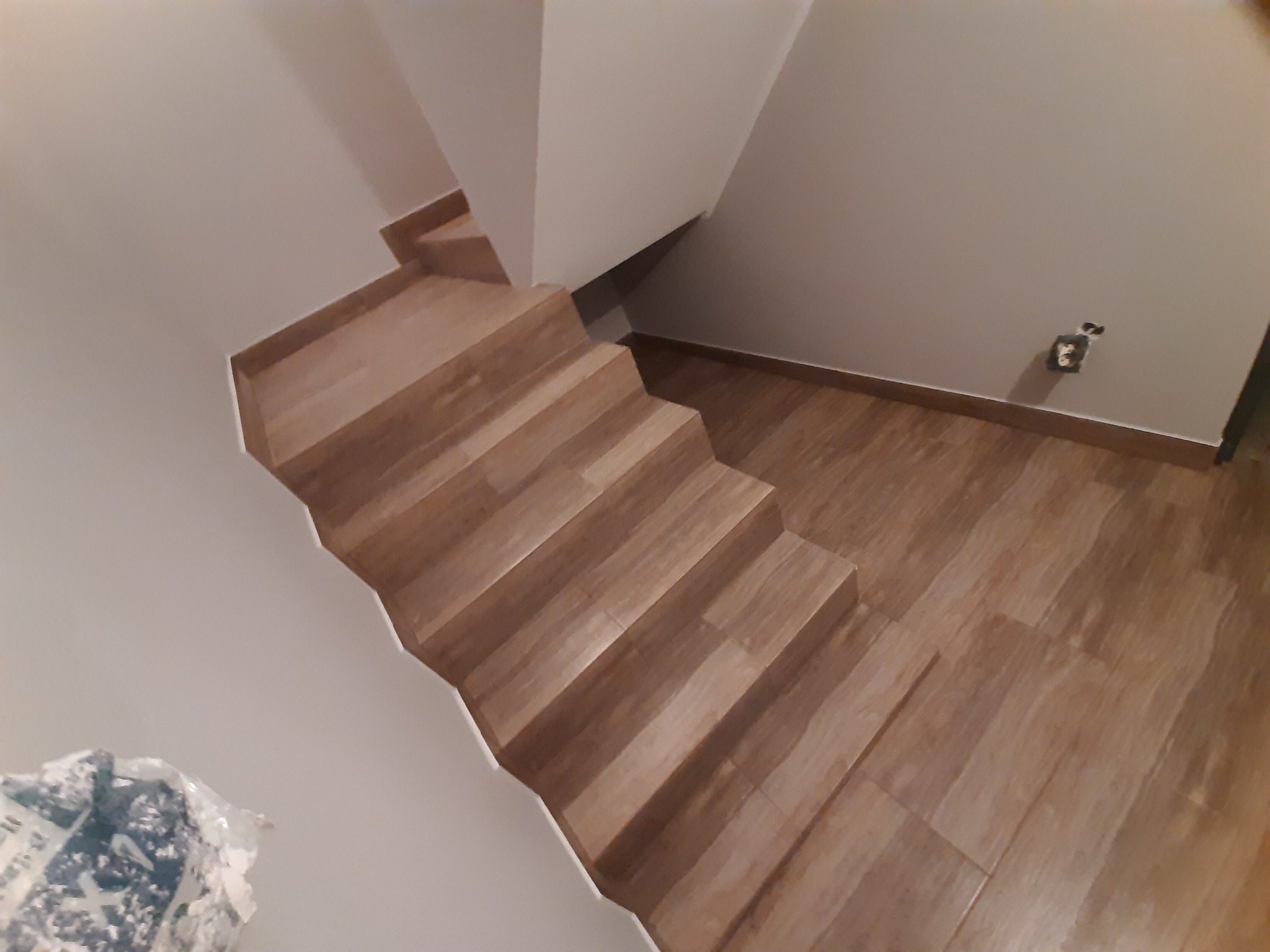 Schody wyłożone panelami imitującymi drewno, widok z góry, częściowo widoczna ściana z gniazdkiem elektrycznym i opakowanie materiałów budowlanych.