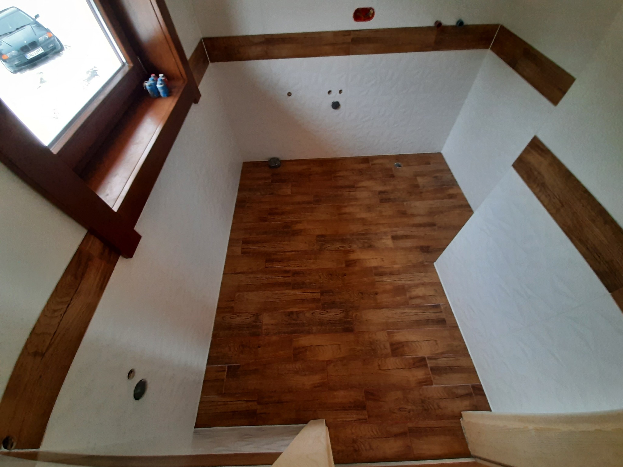 Ściana wyłożona panelami imitującymi drewno, widok z dołu, fragment okna z widocznym samochodem na zewnątrz, drewniane belki stropowe.