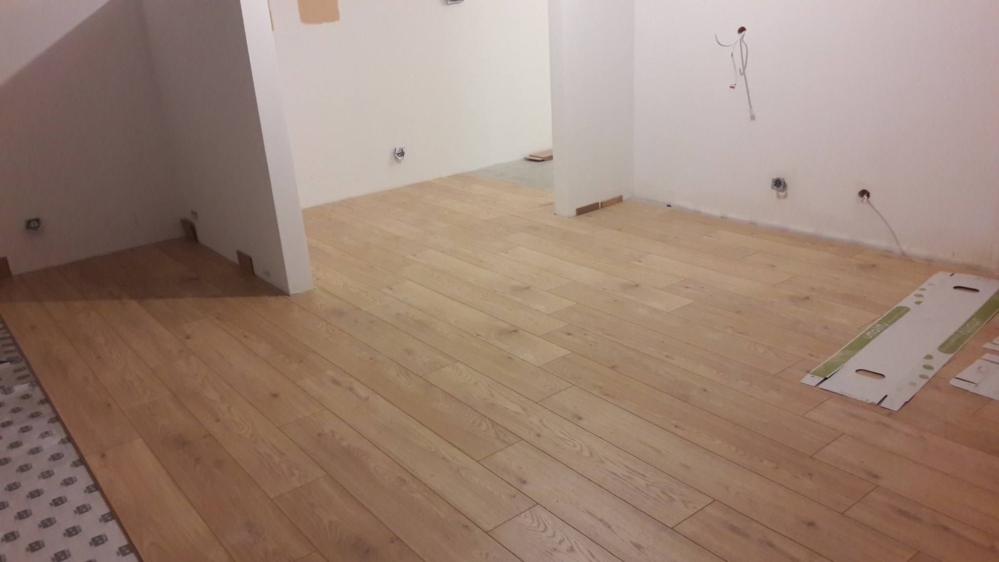 Jasna drewniana podłoga ułożona w nowym pomieszczeniu, widoczne puste puszki elektryczne i fragmenty kartonów po panelach.